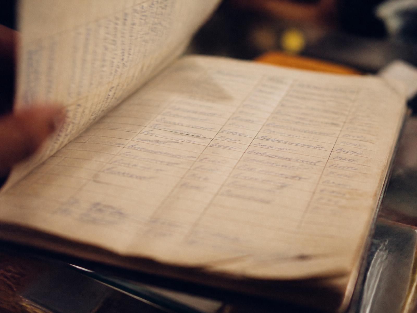 A handwritten paper ledger open on a counter, entries deliberately unreadable